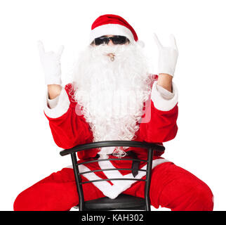 Mann in santa claus Kleidung in einem Stuhl sitzend, die den Rocker hand Zeichen auf weißem Hintergrund Stockfoto