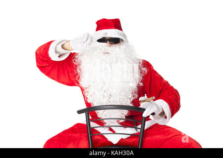 Santa Claus in einem Stuhl sitzend mit Sonnenbrille, die Geste des Tanzens und das Rauchen einer Zigarre auf weißem Hintergrund Stockfoto