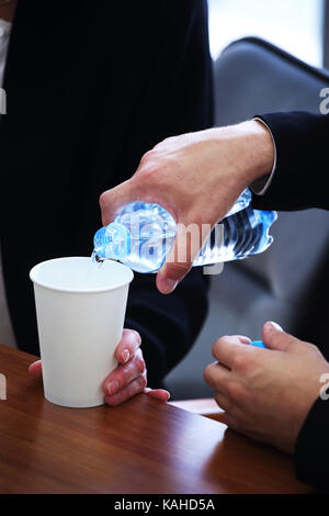 Geschäftsmann im Anzug gießt Wasser aus einer Flasche in Papier Schale an der Konferenz Stockfoto