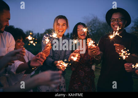 Gruppe von Freunden genießen mit Wunderkerzen. Junge Männer und Frauen genießen mit Feuerwerk. Stockfoto