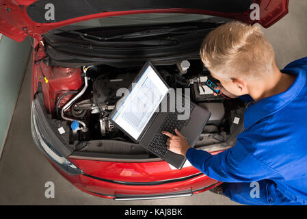 Hohe Betrachtungswinkel und der Mechaniker mit Laptop zur Reparatur Auto in einer Garage. Stockfoto