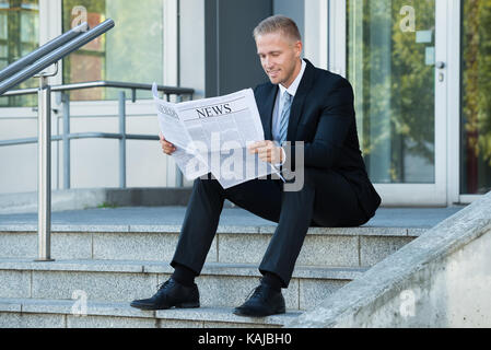 Lächelnde junge Unternehmer lesen Zeitung sitzen auf Treppen Stockfoto