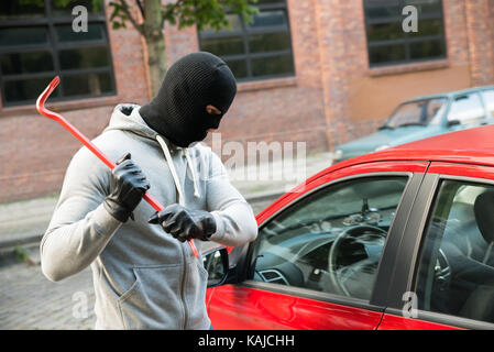 Dieb mit Maske Versuchen, das Fenster zu Smash des Auto mit Brecheisen Stockfoto