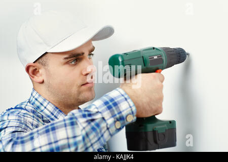 Junge Arbeitnehmer Mann mit Bohrmaschine und Loch in weiße Wand Stockfoto