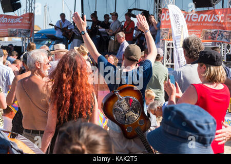 Der Mann mit der Dobro-gitarre auf seinem Rücken an den Gitarren am Strand Veranstaltung in Lyme Regis, Dorset, Großbritannien. Stockfoto