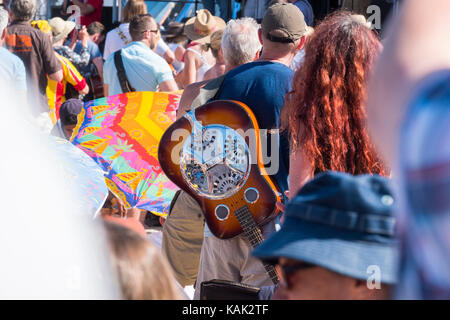 Mann mit Dobro-gitarre auf seinem Rücken an den Gitarren am Strand Veranstaltung in Lyme Regis, Dorset, Großbritannien. Stockfoto