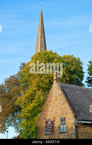 Bloxham Village Museum und Bäume im Herbst vor der Kirche, Turm gegen einen strahlend blauen Himmel im September. Bloxham, Oxfordshire, England Stockfoto