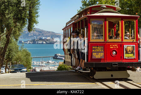 Cable Car über die Hügel in Richtung Insel Alcatraz in San Francisco, Kalifornien, USA zu sinken. Menschen reiten in der Seilbahn. Alcatraz in der Ferne zu sehen. Stockfoto