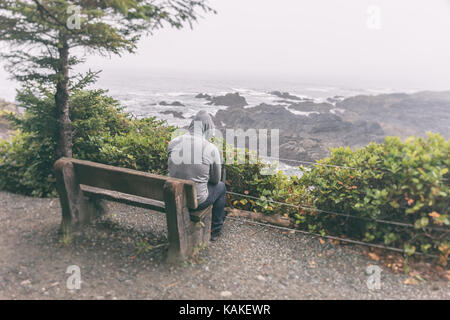 Traurig und einsam Mann sitzt auf der Bank mit Blick auf das Meer auf Vancouver Island Stockfoto