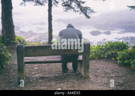 Traurig und einsam Mann sitzt auf der Bank mit Blick auf das Meer auf Vancouver Island Stockfoto