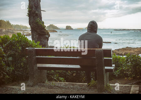 Traurig und einsam Mann sitzt auf der Bank mit Blick auf das Meer auf Vancouver Island Stockfoto