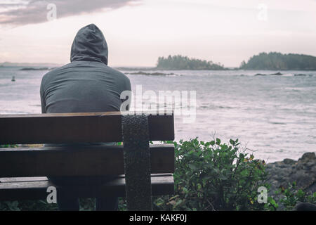 Traurig und einsam Mann sitzt auf der Bank mit Blick auf das Meer auf Vancouver Island Stockfoto