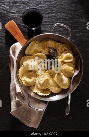 Gekocht serviert pan Ravioli mit Parmesan und gebratenem Salbei. Auf schwarzen Stein Hintergrund mit Glas Rotwein Stockfoto
