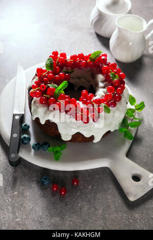 Bundt Cake mit frischen Beeren und Sauce aus saurer Sahne am grauen Stein Tabelle Stockfoto