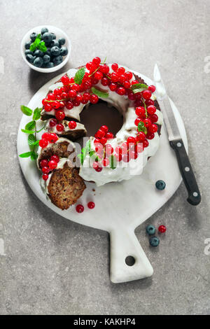 Bundt Cake mit frischen Beeren und Sauce aus saurer Sahne am grauen Stein Tabelle Stockfoto