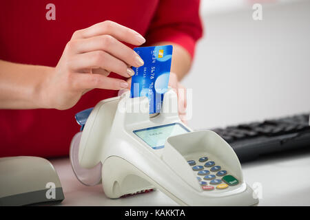 Mittelteil der Verkäuferin streichen Kreditkarte auf Reader bei Store Stockfoto