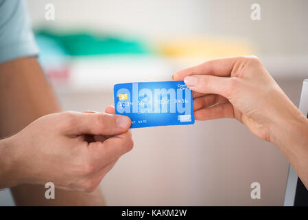 Zugeschnittenes Bild der Verkäufer die Kreditkarte von weiblichen Kunden in Clothing Store Stockfoto