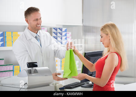 Lächelnd Apotheker Arzneimittel zu geben, weibliche Kunden am Counter in Store Stockfoto