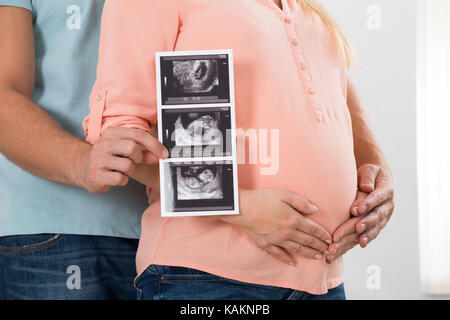 Mittelteil des Menschen zeigen Ultraschall Bericht scan beim Stehen mit schwangeren Frau zu Hause Stockfoto