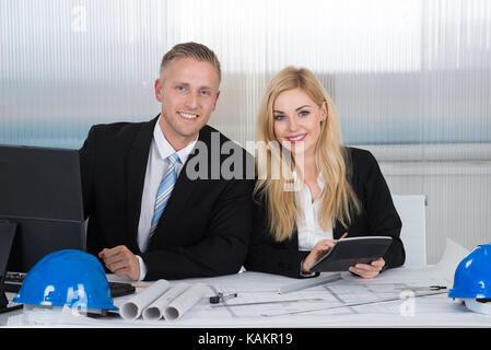 Selbstbewussten jungen Architekten diskutieren über Blueprint am Schreibtisch im Büro Stockfoto