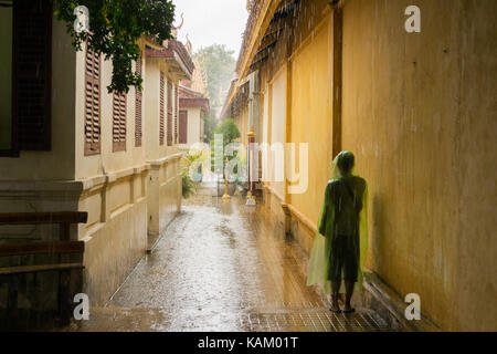 Ein Jugendlicher, der ein transparent grün regen Jacke, für die schweren Monsunregen während ein heftiger Regenschauer in Phnom Penh, Kambodscha zu stoppen. Stockfoto