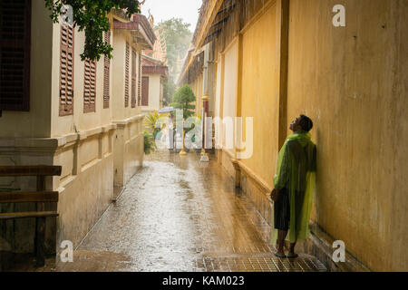 Ein Jugendlicher, der ein transparent grün regen Jacke, für die schweren Monsunregen während ein heftiger Regenschauer in Phnom Penh, Kambodscha zu stoppen. Stockfoto