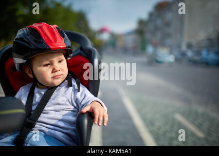 Familie Radfahren in der Stadt. Wenig schöne Mädchen Helme tragen im Fahrrad Sitz. Stockfoto