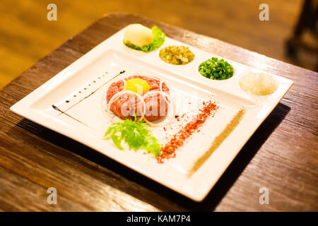 Das leckere Essen von rohem Fleisch und Eidotter mit grünen, Gewürze und Zwiebeln. Die seitliche Ansicht. Stockfoto