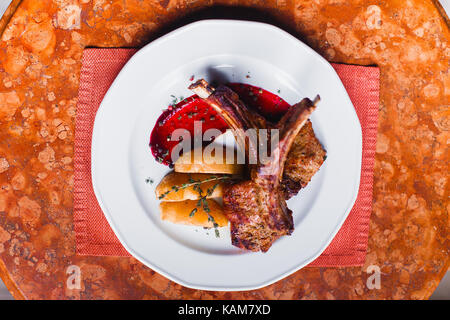 Die close-up oben Blick auf die Zusammensetzung von Lebensmitteln. Die Platte voller gebratene Rippen und Kartoffeln mit roter Soße. Stockfoto