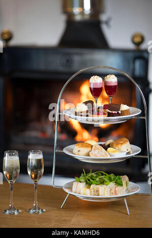 Nachmittagstee platter vor einem prasselnden orange warmen Kaminfeuer serviert. Stockfoto