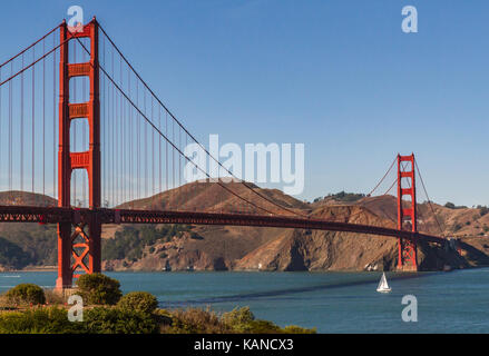 Golden Gate Bridge, San Francisco, Kalifornien, USA. Einzelne weiße Segelboot über die unter der Brücke. Platz für Kopie in blauer Himmel, keine Wolken. Stockfoto