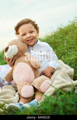 Ein junger spanischer Junge mit Teddybär sitzen auf Gras Stockfoto