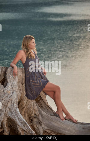Eine junge Frau auf einem Baumstumpf neben einem kleinen Bergsee