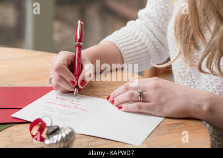 Junge Frau Schreiben von Weihnachtskarten mit Rote nägel, einen roten Stift und Urlaub Dekorationen auf einer hölzernen Tisch Stockfoto