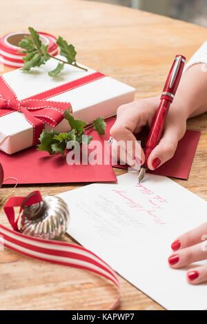 Junge Frau Schreiben von Weihnachtskarten mit Rote nägel, einen roten Stift und Urlaub Dekorationen auf einer hölzernen Tisch Stockfoto