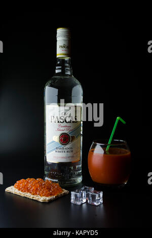 Tiraspol, Moldau - Juni 5, 2016: Karibik weisser Rum old pascas Flasche auf einem schwarzen Hintergrund mit rotem Kaviar Toast, Eiswürfel und ein Glas Blut ma Stockfoto