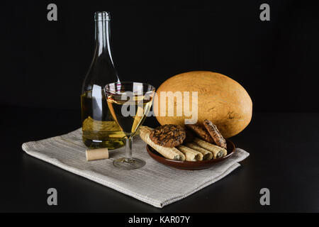 Flasche Weißwein, Melone, Ton Platte von Süßigkeiten und einem Glas Wein auf einem schwarzen Hintergrund Stockfoto