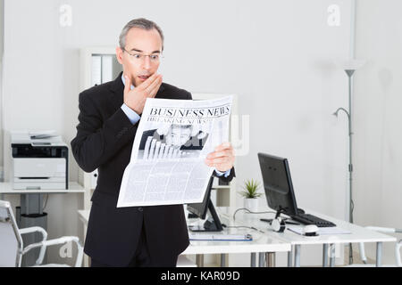 Reifen Geschäftsmann lesen Zeitung beim Stehen in der Office Schockiert Stockfoto