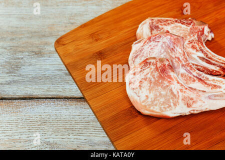 Schweinesteak auf einem Holzbrett Schweinekoteletts auf einem Schneidebrett. Selektiver Fokus Stockfoto