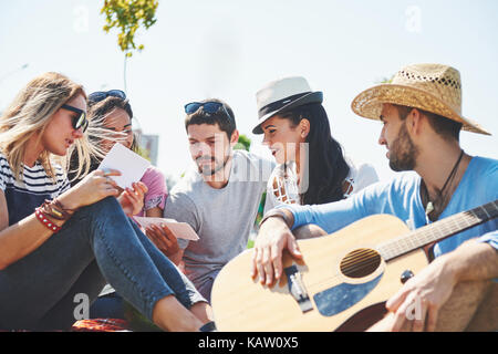 Glückliche junge Freunde mit Picknick im Park. Sie alle sind glücklich, Spaß, lächelnd und Gitarre spielen Stockfoto