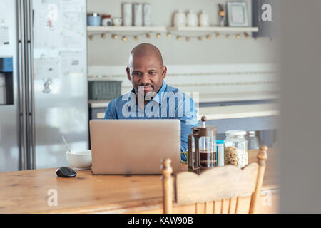 Lächelnd reife afrikanischer Mann mit einem Laptop über Frühstück Stockfoto