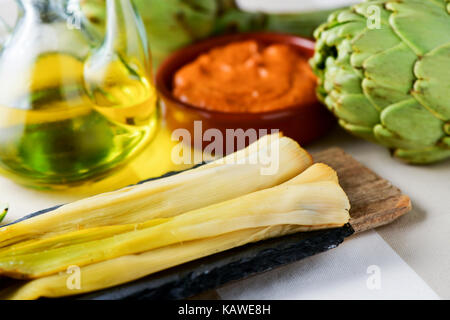 Einige geröstete Calcots, typisch für Katalonien, Spanien und eine Steingut-Schale mit Romesco-Sauce, Tauchen sie in ihm, und eine Menage mit Oliven o süße Zwiebeln Stockfoto