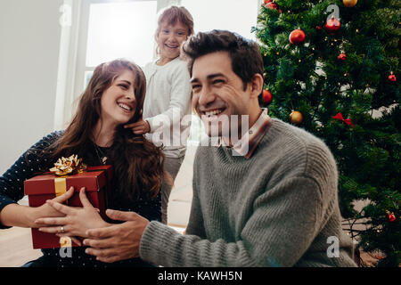 Happy Family den Austausch von Geschenken sitzen neben einem Weihnachtsbaum. Lächelnde junge Frau mit einem Geschenk zu Weihnachten. Stockfoto