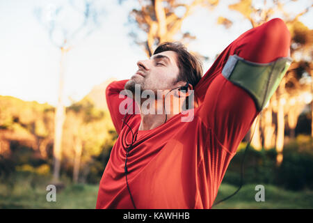 Runner Atemübungen, während Sie Musik hören in einem Park. Mann entspannt mit geschlossenen Augen nach dem Workout. Stockfoto