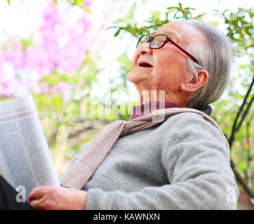 Eine glückliche hochrangigen chinesischen Frau liest Buch im Hof Stockfoto