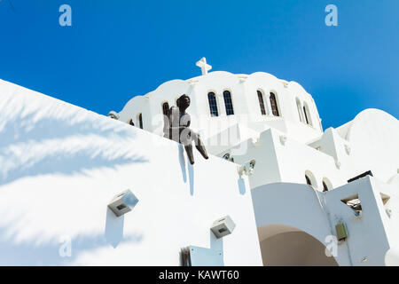Eine kleine Bronzeskulptur eines Mann sitzt auf dem Dach des Griechisch-orthodoxe Kathedrale von ypapanti in Fira Dorf auf der Insel Santorin, Griechenland Stockfoto