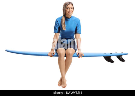 Junge Frau in einem Neoprenanzug sitzen auf Surfbrett und lächelnd auf weißem Hintergrund Stockfoto