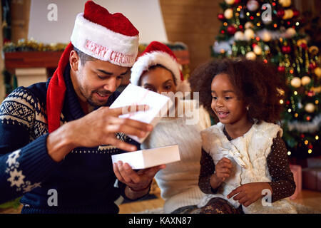 Familie mit schwarzen Kind neugierig betrachten Open Box mit Weihnachtsgeschenk Stockfoto
