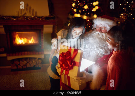 Santa Claus mit Magic vorhanden mit Neugier Kinder umgeben Stockfoto