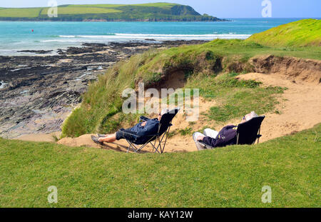 Reifer Mann und Frau Zuflucht von der Wind in den Dünen während Sie die Strahlen der Sonne an daymer Bay, Cornwall, England, Großbritannien Stockfoto